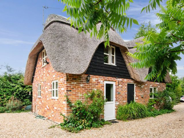 A thatched roof cottage with garden and gravel pathway at Walnut Tree Cottage 