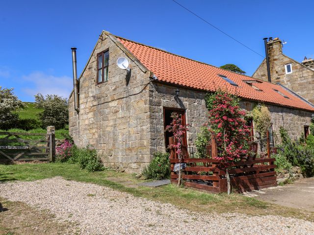 A stone cottage with a red tiled roof and a small wooden fenced patio with plants and flowers at Wildflower Cottage in Danby