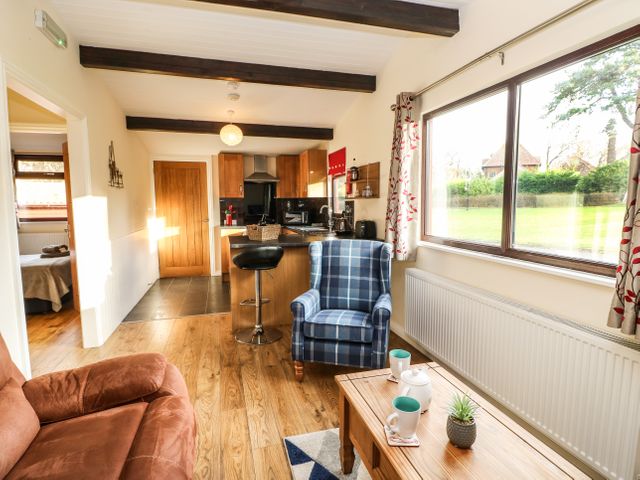 A living room with a brown sofa and blue plaid armchair next to a wooden coffee table and large window at Primrose Lodge in Saltburn-by-the-Sea