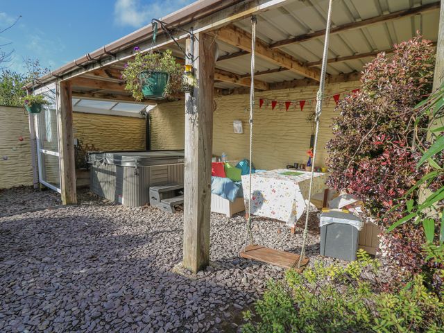 An outdoor covered patio area with a swing a hot tub hanging plants a table with a tablecloth and cushions at Yr Hen Llaethdy Blaen-Cil-Llech near Newcastle Emlyn