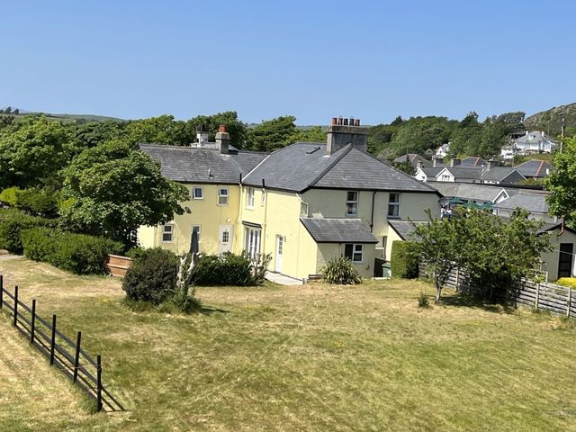 A yellow two story house with multiple chimneys surrounded by trees and grass at Gwelfor in Morfa Bychan