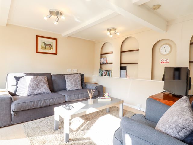 A living room with grey sofas a coffee table a television and shelves with books at Vine Cottage in Castle Hedingham