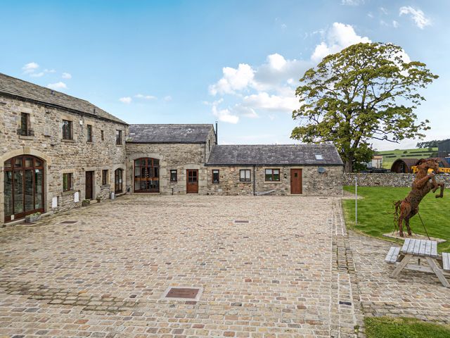 An outdoor courtyard with stone buildings and a sculpture at Orcaber Farm Barn in Austwick near Settle