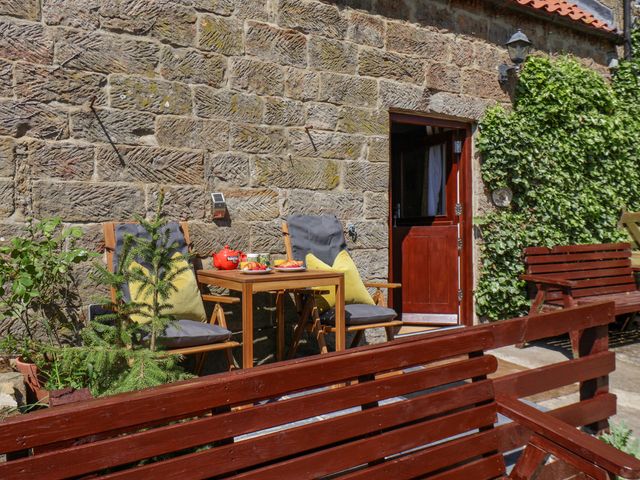 A patio with a wooden table and cushioned chairs outside a stone building with a door and climbing plants at Daffodil Cottage in Houlsyke near Danby