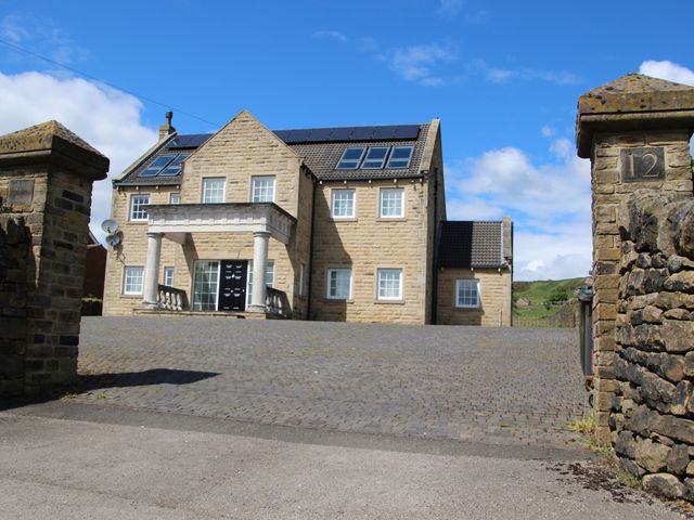 A large stone house with multiple windows and solar panels on the roof behind stone pillars at Hartcliffe View in Millhouse Green