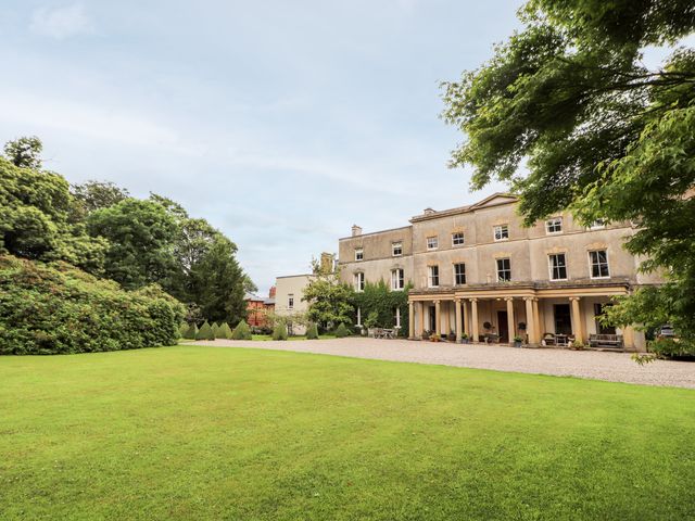 A large historic building with columns and multiple windows surrounded by a lawn and trees at Cooks Flat in Cefn Park