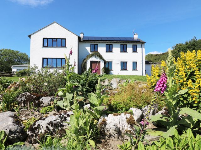 A white two-story house with several windows and a front door surrounded by greenery and colorful flowers at Ghyll Bank House in Staveley near Windermere