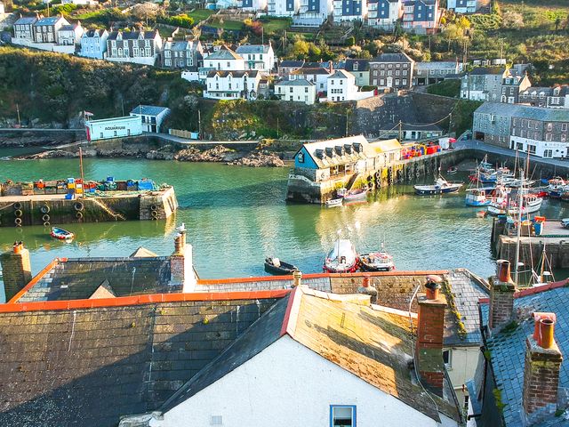 A coastal harbor with boats docked and houses on a hillside at Thimble Cottage in Mevagissey