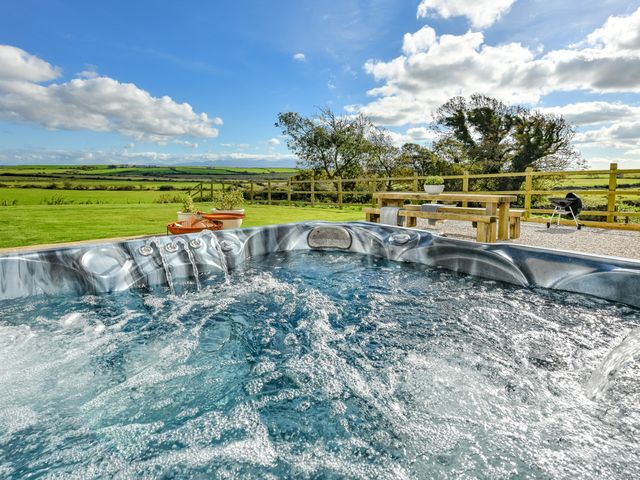 An outdoor hot tub with water flowing and bubbles in a garden with a wooden picnic table and barbecue at Ty Carmel in Rhosneigr