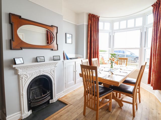 A dining room with a wooden table and six chairs near a bay window and a white fireplace at Glandwr in Borth-y-Gest