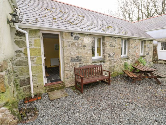 An outdoor area with a stone building a wooden bench and a wooden picnic table at Swallows in St Keverne Lizard Peninsula