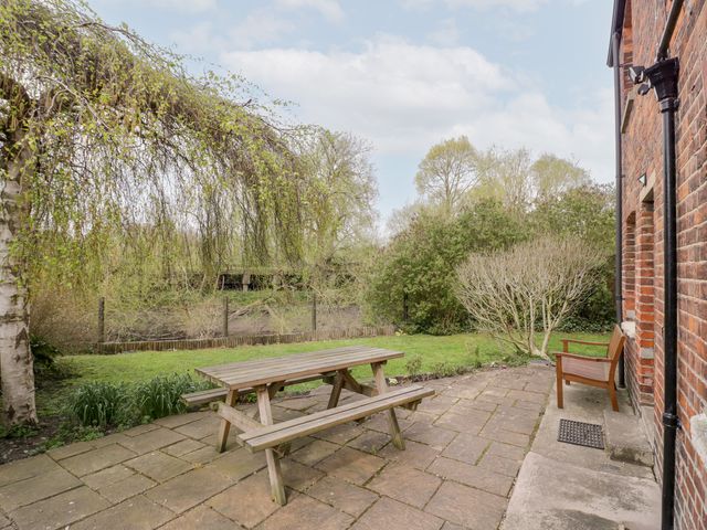 A patio with a wooden picnic table and bench next to a brick house with a wooden chair and garden at The Lock House Gloucester