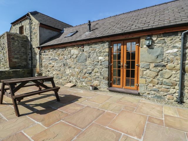 An outdoor area with a wooden table and stone walls at Lily Cottage in Caeathro near Caernarfon