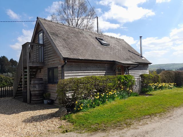 A wooden cottage with stairs and a small balcony surrounded by bushes and flowers at Bicton Lodge in Clun