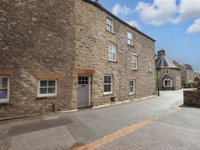 A stone building with a front door in a pedestrian area at Back Cottage in Kirkby Lonsdale
