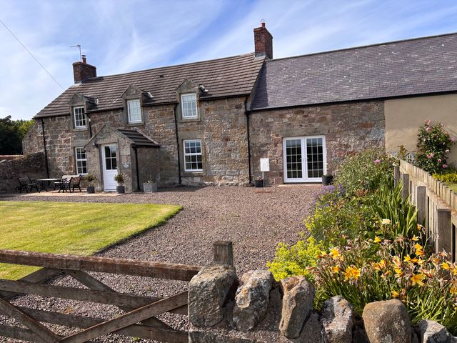 An outdoor view of a house with a lawn and flower bed at The Old Farmhouse in Lowick