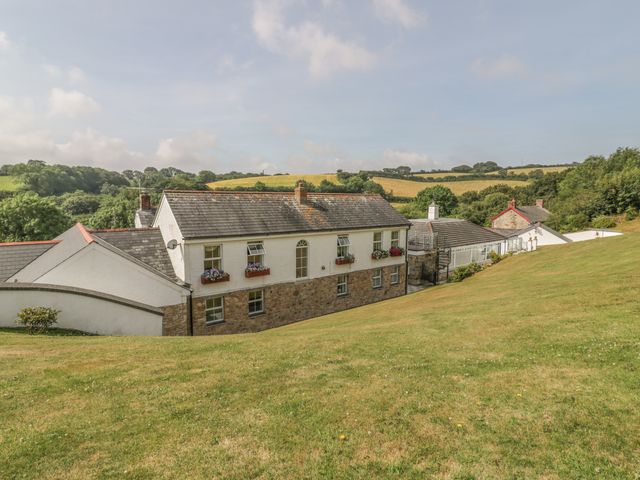 A stone and white house with flower boxes on windows surrounded by a grassy hill and countryside at Chapel Green in Polgooth