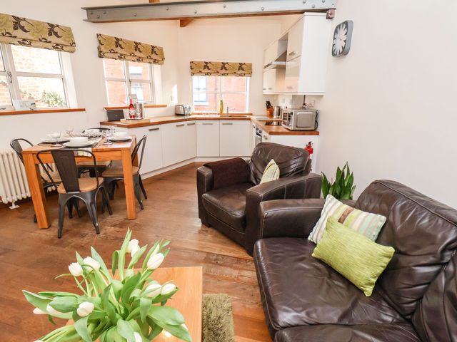 A living room and kitchen area with a brown leather sofa and armchair a wooden dining table with metal chairs and white cabinets at The Old Blacksmith's Workshop in Whitby
