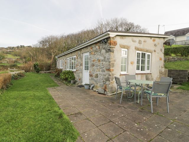 A stone cottage with a patio table and four chairs on a paved area next to a grass lawn at Hen Felin Isaf in Llanddona near Beaumaris