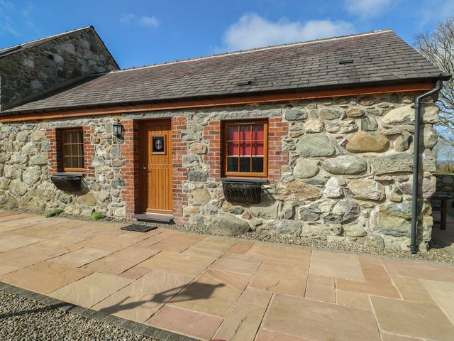 A stone cottage exterior with a wooden door and windows at Poppy Cottage in Caeathro near Caernarfon