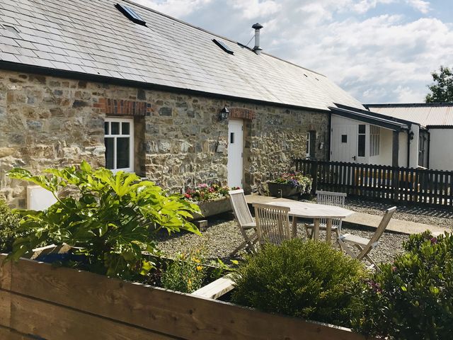 An outdoor area with stone walls, a patio table and chairs at Bwthyn Bach in Newport