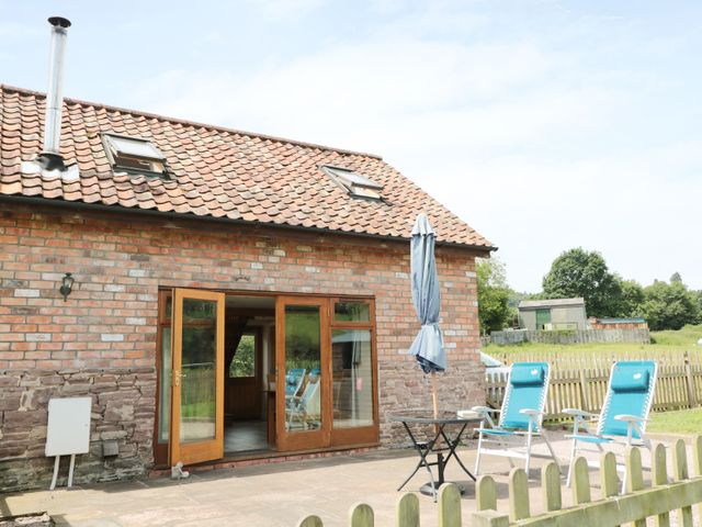 A brick building with a tiled roof and open wooden doors leading to a patio with blue chairs and a closed patio umbrella at Mallard in Newnham-on-Severn near Gloucester 