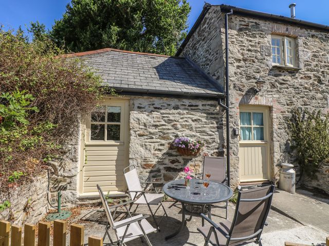 A stone cottage exterior with two beige doors a round glass table with four chairs and flowers at Honeycrock in Crantock near Newquay