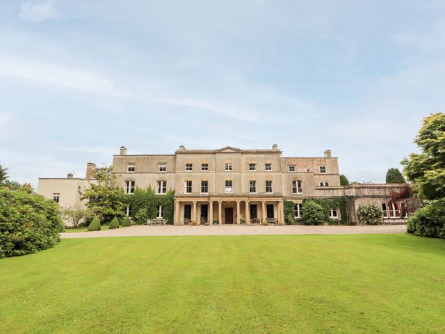 A large historic building with columns and multiple windows surrounded by green lawn and trees at Butlers Flat in Cefn Park