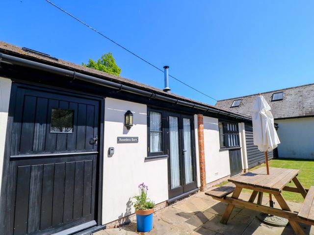Exterior view of a building with black doors and windows a wooden picnic table and umbrella on a patio at Rowdens Barn in Winterborne Stickland