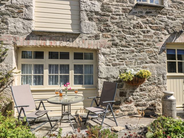 A stone wall exterior with two chairs and a table with drinks and flowers a flower basket on the wall and a metal milk container outside at Trevena Crantock near Newquay