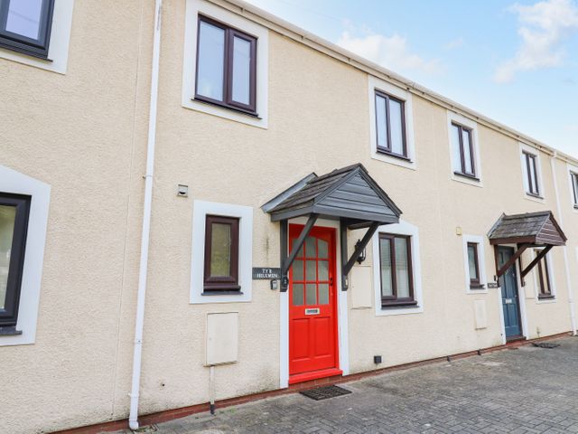 The exterior of a beige terraced house with a red door and multiple windows at Ty'r Heulwen in Aberdovey