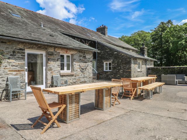 An outdoor patio area with wooden tables and chairs outside a stone house at Jubilee in Graythwaite near Hawkshead