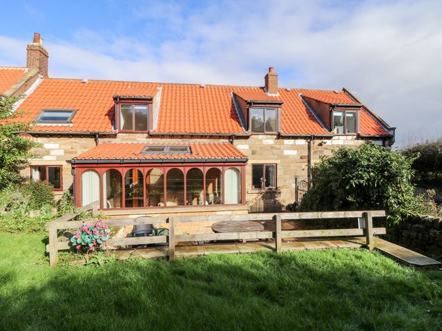A stone house with red tiled roof and a glass conservatory overlooking a garden with grass and wooden fence at Airy Hill Farm Cottage in Whitby