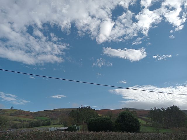 A rural landscape with hills trees and a few buildings under a blue sky with scattered clouds at Plas Glyndwr in Crickhowell