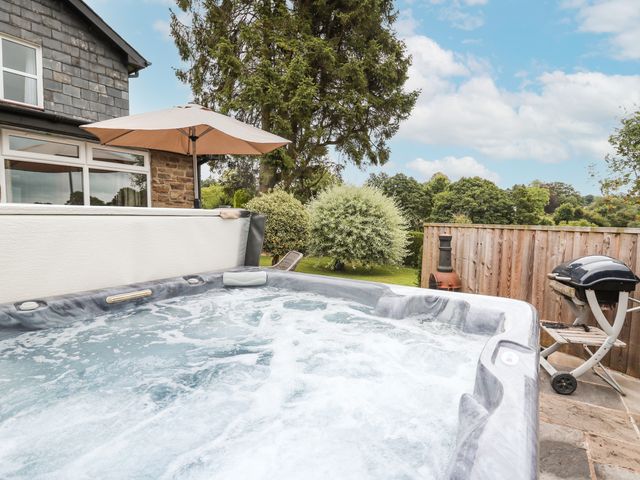 An outdoor hot tub with bubbling water near a house with an umbrella and barbecue grill at Holly Farm Cottage in Howey
