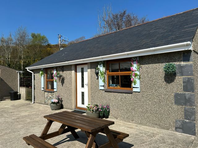 Exterior view of a single-story building with a white door two windows and a wooden picnic table outside at The Mill in Abererch near Pwllheli