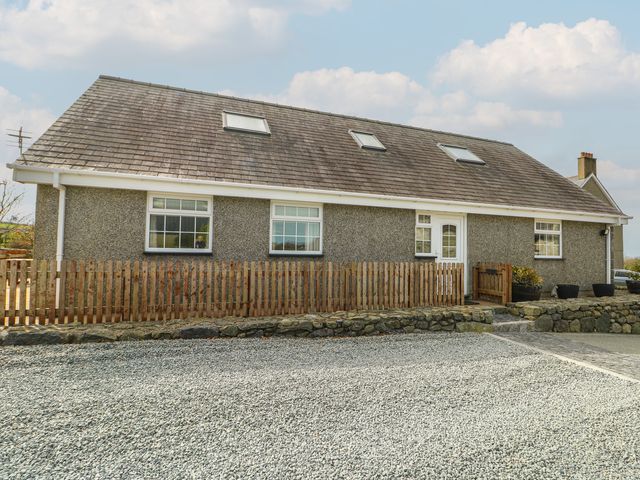 A house with a gravel driveway and a wooden fence at Ty Ni Caeathro near Caernarfon