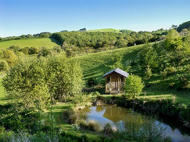 A small wooden cabin near a pond with trees and hills in the background at Black Mountain View in Llanafan Fawr near Builth Wells