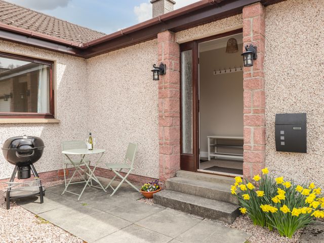 An outdoor patio area with a small table and two chairs a black barbecue grill and yellow flowers near the steps to a house entrance at Millview in Boat of Garten