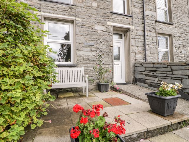 A stone house exterior with a white bench near a window and two flower pots on the pavement at Ty Gwynn in Tanygrisiau
