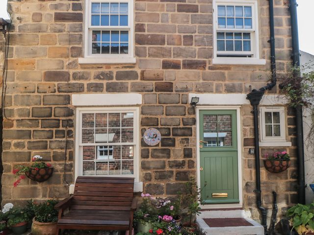 A stone exterior wall with windows and a green front door at Bulmers Cottage in Staithes
