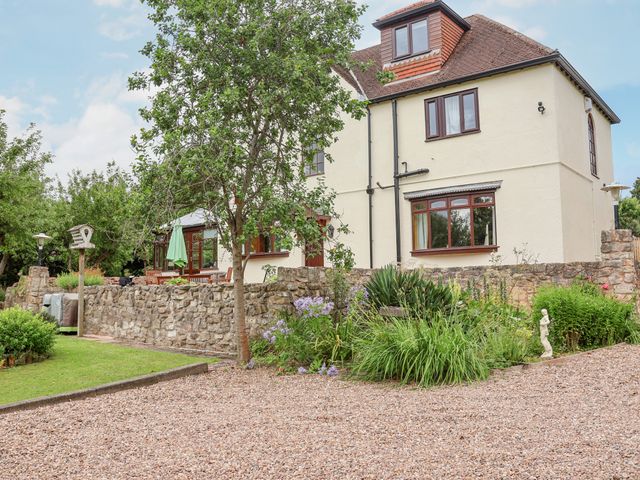 An exterior view of a multi-story house with a stone wall and garden with plants and a tree at Pringles Orchard in Carlton-in-Lindrick