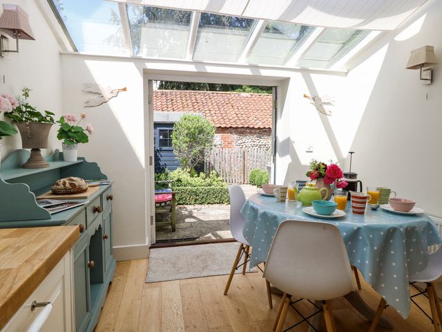 A dining area with a round table covered by a blue polka dot tablecloth and chairs under a glass roof at Bridge Cottage in Aylsham