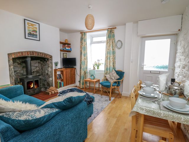 A living room with a fireplace a blue sofa a wooden dining table set and a window with patterned curtains at Rowan Cottage in Builth Wells