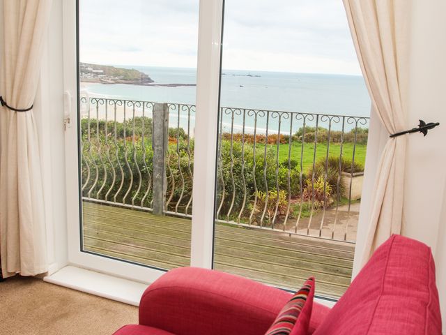A red sofa facing a glass door with beige curtains and a view of a balcony and the sea at The Lookout in Sennen