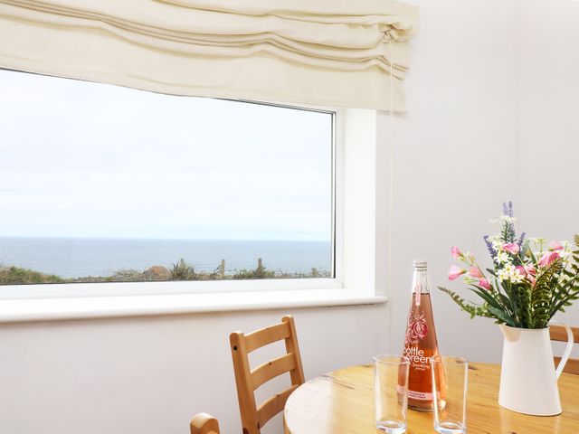 A dining table with a bottle and two glasses near a window with ocean view and flowers in a white pitcher at The Coach House in Sennen near St Just