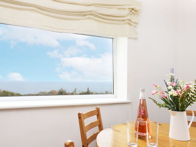 A dining room with a table, chairs, flowers, and a bottle of beverage at The Coach House in Sennen near St Just