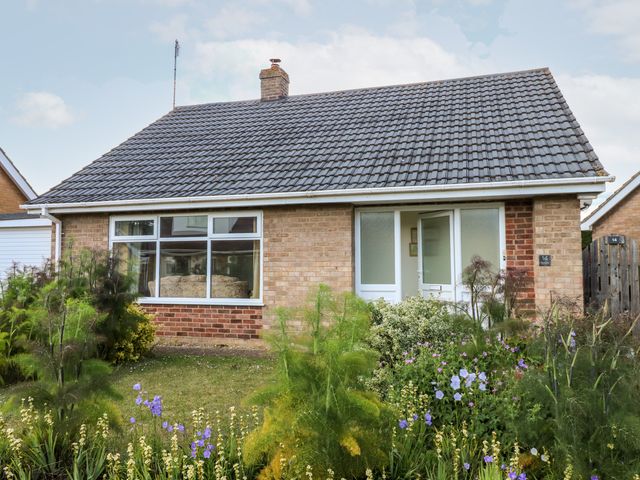 A brick bungalow with a tiled roof and a garden with flowers at Newby in Gayton near Kings Lynn