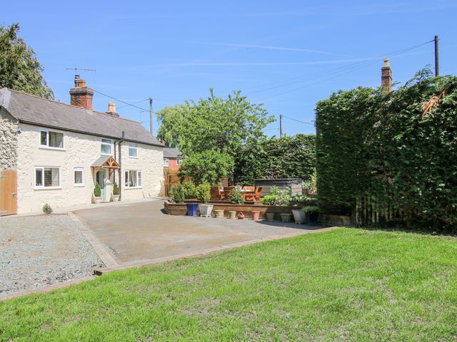 A white cottage with a gravel driveway wooden seating area and hedges at Pennal Cottage in Maesbury Marsh near Knockin
