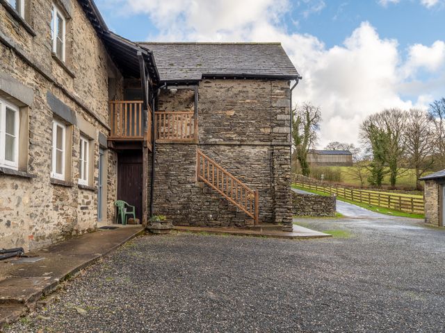 A stone building with wooden stairs and railings outside near a gravel parking area with a green plastic chair at Ullswater in Sawrey